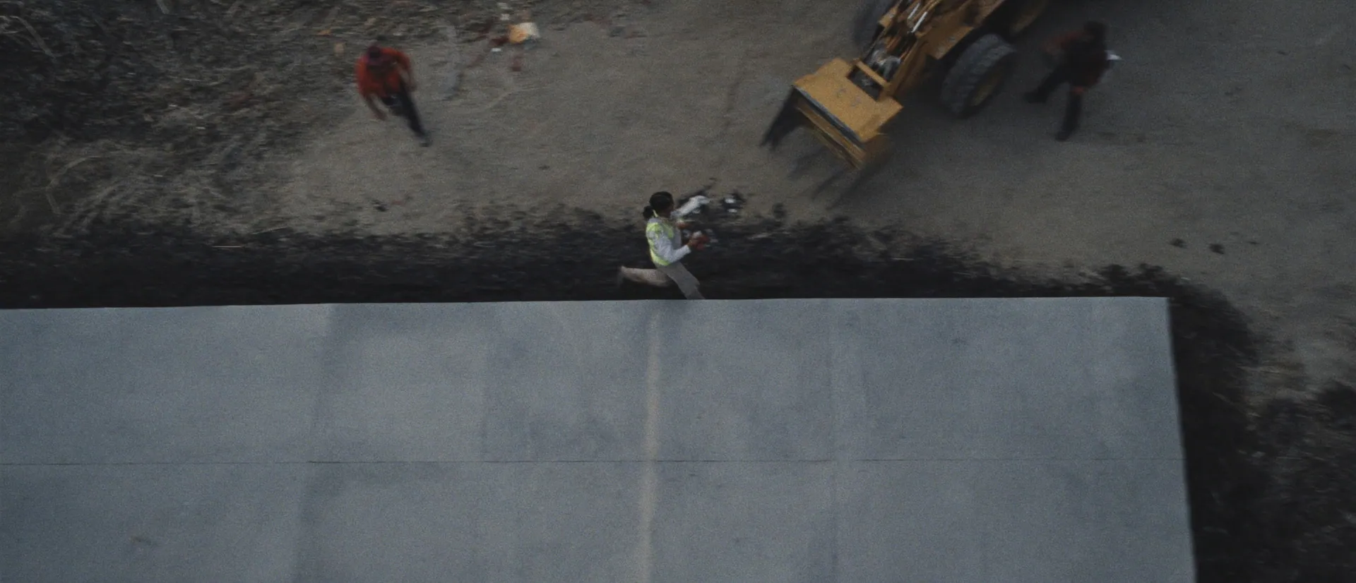 Top-down view of a poured slab beside a loader and workers