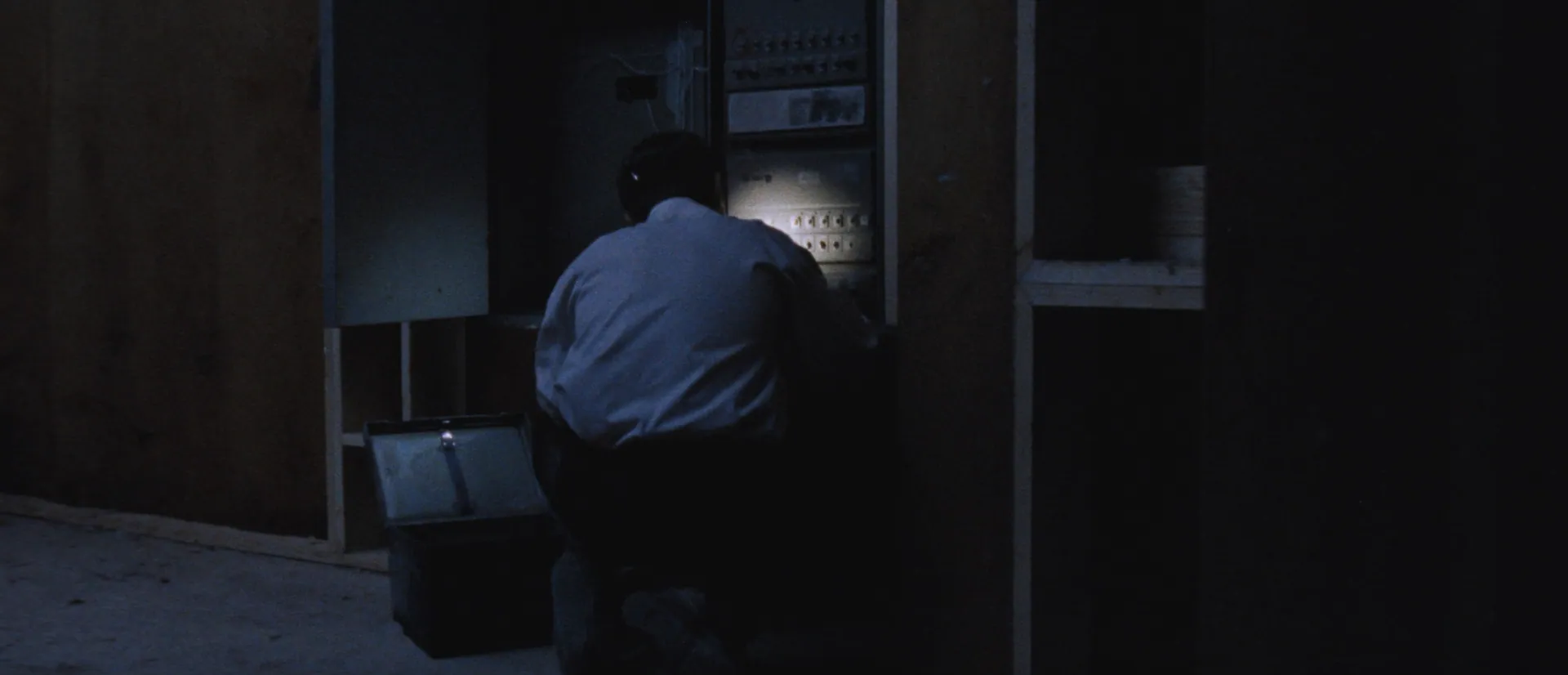 Electrician crouched at a switchboard by head torch