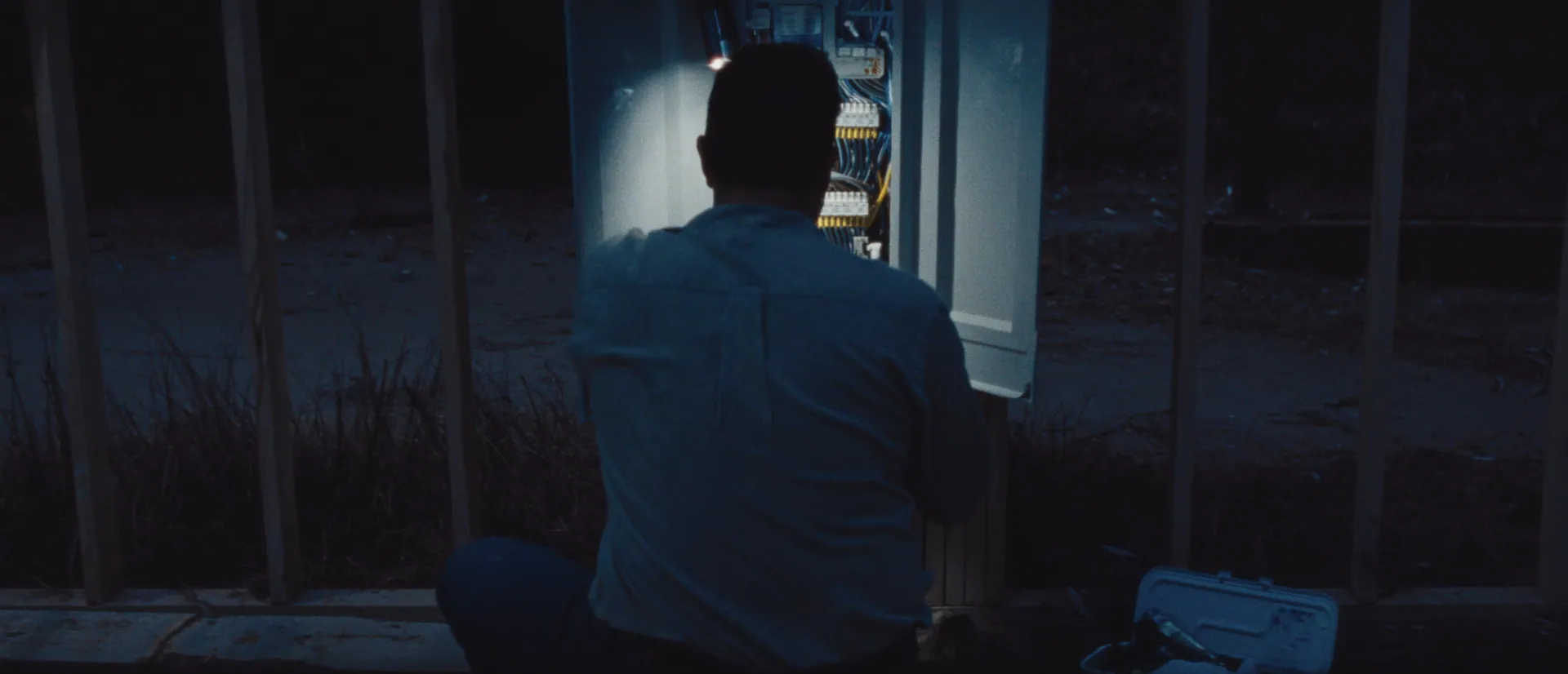 Electrician working at an open switchboard in a house frame at dusk